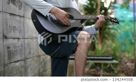 Black Acoustic Guitar With Gray Shirt Hand Playing, Against Gray Wall Green Outdoor Background, Alternative Sound 134244508