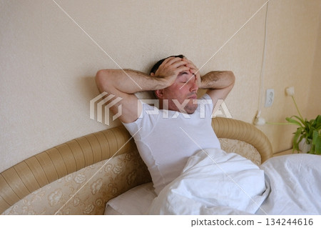 A man holds his head and yawns in bed Man with blanket cover his head feel sleepy and yawn close the eye on white isolated background A man holds his head and yawns in bed Man with blanket cover his head feel sleepy and yawn close the eye on white isolated background 134244616