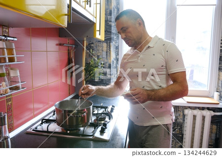 Man cooking kitchen with pan at kitchen. Chef cook prepares with pan. Chef cooking with pan in modern kitchen. Mature chef man hold pan standing in kitchen, preparing food. 134244629