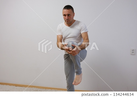 Smiling fit senior sportsman stretching his leg on a bridge and doing warmup exercises. 134244634