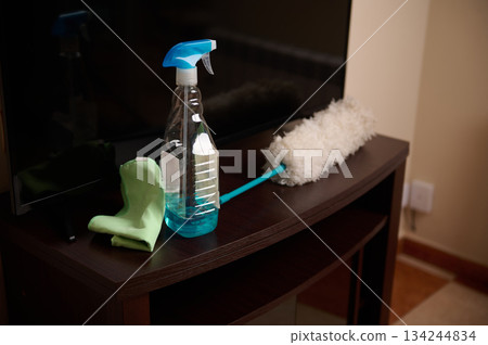 Cleaning Supplies On Wooden TV Stand With Spray Bottle, Glove, And Mop In Living Room Cleaning Supplies On Wooden TV Stand With Spray Bottle, Glove, And Mop In Living Room 134244834