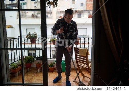Man Cleaning Balcony With Mop On Terrace, Plants Nearby, Quiet Home Scene Man Cleaning Balcony With Mop On Terrace, Plants Nearby, Quiet Home Scene 134244841