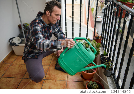 Man Watering Plants On Balcony With Green Watering Can Amid Potted Succulents 134244845