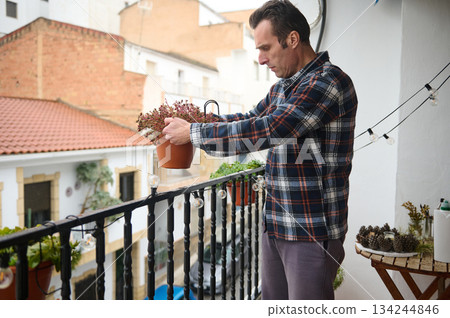 Man On Balcony Plant Potting On A Cozy Urban Terrace With String Lights 134244846