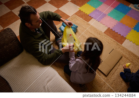 Father And Child Unpack Gift Bag While Playing On Colorful Foam Mat At Home Father And Child Unpack Gift Bag While Playing On Colorful Foam Mat At Home 134244884