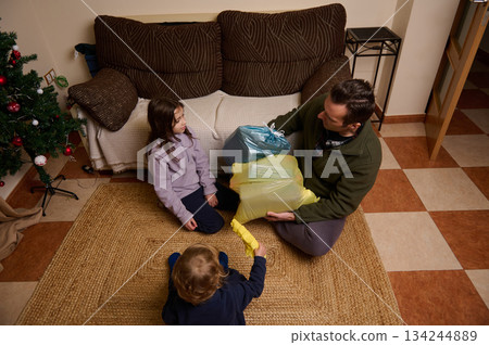 Family Christmas Gift Exchange At Home With Father And Children On Rug In Living Room Family Christmas Gift Exchange At Home With Father And Children On Rug In Living Room 134244889