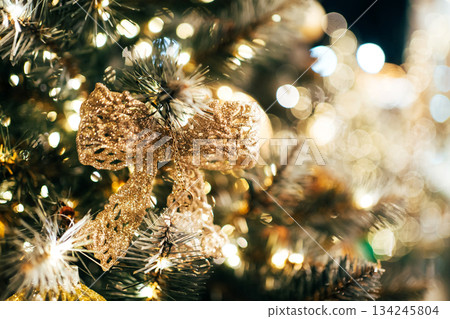 Golden glitter bow decorating a festive christmas tree bokeh lights 134245804