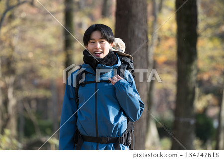 A young man climbing a mountain surrounded by autumn and winter foliage, looking at the camera. Image of outdoor outings and leisure activities. A young man climbing a mountain surrounded by autumn and winter foliage, looking at the camera. Image of outdoor outings and leisure activities. 134247618