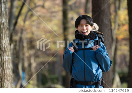 一位年輕男子攀登一座被秋冬樹葉環繞的山峰,他看向鏡頭。這是戶外郊遊和休閒活動的畫面。 一位年輕男子攀登一座被秋冬樹葉環繞的山峰,他看向鏡頭。這是戶外郊遊和休閒活動的畫面。 134247619
