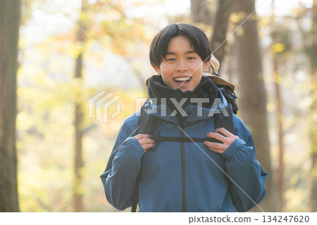 一位年輕男子攀登一座被秋冬樹葉環繞的山峰,他看向鏡頭。這是戶外郊遊和休閒活動的畫面。 一位年輕男子攀登一座被秋冬樹葉環繞的山峰,他看向鏡頭。這是戶外郊遊和休閒活動的畫面。 134247620