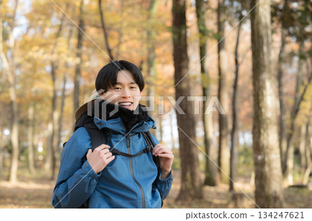 A young man climbing a mountain surrounded by autumn and winter foliage, looking at the camera. Image of outdoor outings and leisure activities. 134247621