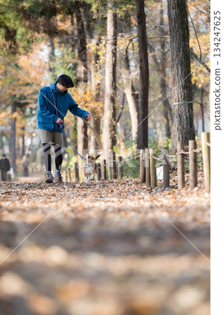 一位微笑的男子在秋日的公園帶著他的狗散步,享受著與寵物相處的時光。 一位微笑的男子在秋日的公園帶著他的狗散步,享受著與寵物相處的時光。 134247625