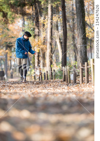 一位微笑的男子在秋日的公園帶著他的狗散步，享受著與寵物相處的時光。 134247626