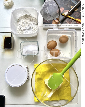 Various baking tools and ingredients arranged neatly, including whisk, rolling pin, measuring cups, flour, eggs, butter, and sugar, showcasing smooth textures and organized setup in close-up detail 134247877