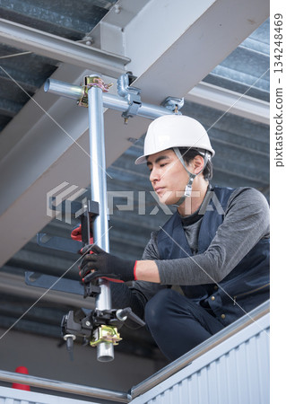 Construction work such as clamping to fix single pipes on high scaffolding near the ceiling. Image of construction workers and workers tightening with wrenches. Construction work such as clamping to fix single pipes on high scaffolding near the ceiling. Image of construction workers and workers tightening with wrenches. 134248469