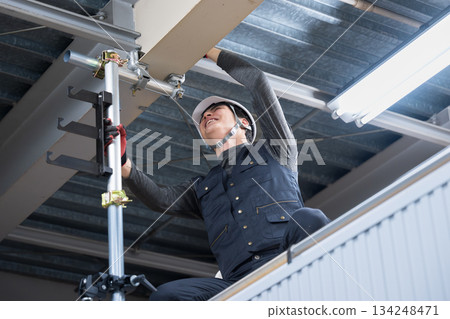 Construction work such as clamping to fix single pipes on high scaffolding near the ceiling. Image of construction workers and workers tightening with wrenches. 134248471