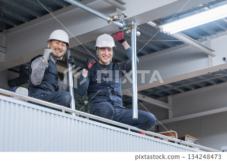 施工場景包括將單管管道固定在靠近天花板的高鷹架上。圖中是鷹架工人和工作人員，他們面帶微笑。 134248473