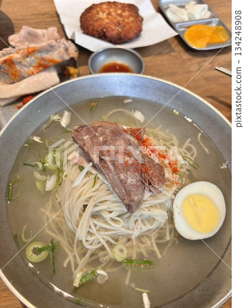 Authentic Pyongyang naengmyeon with chewy buckwheat noodles in cold, clear broth, offering a refreshing and delicate flavor. Perfect for traditional Korean cuisine menus and summer dishes. Authentic Pyongyang naengmyeon with chewy buckwheat noodles in cold, clear broth, offering a refreshing and delicate flavor. Perfect for traditional Korean cuisine menus and summer dishes. 134248908
