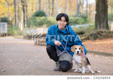 一位微笑的男子在秋日的公園裡遛狗,享受著與愛犬相處的時光,並看向鏡頭。 一位微笑的男子在秋日的公園裡遛狗,享受著與愛犬相處的時光,並看向鏡頭。 134248954