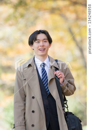 一位身穿外套的男士在秋葉環繞下外出辦事。 134248958