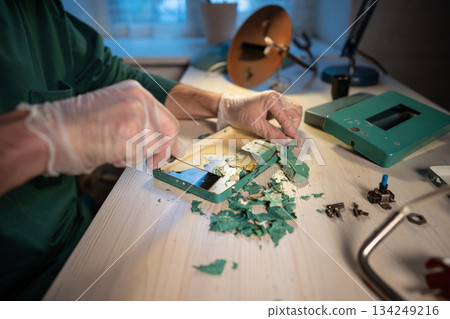 Craftsman with putty knife tool precisely removing dry layers of paint from inside of base part. 134249216