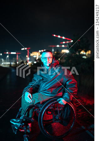 Man with disability in wheelchair in red blue rgb color light on late night walk alone in urban city Man with disability in wheelchair in red blue rgb color light on late night walk alone in urban city 134249217
