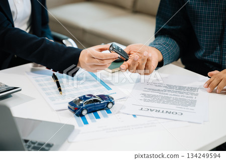 Business professionals finalize a car sale agreement with paperwork and model car, capturing themes 134249594