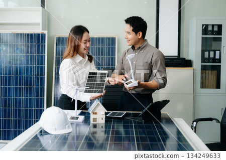 Two Asian engineers collaborate on a solar and wind energy project, discussing innovation and sustainability in a modern office setting. Two Asian engineers collaborate on a solar and wind energy project, discussing innovation and sustainability in a modern office setting. 134249633