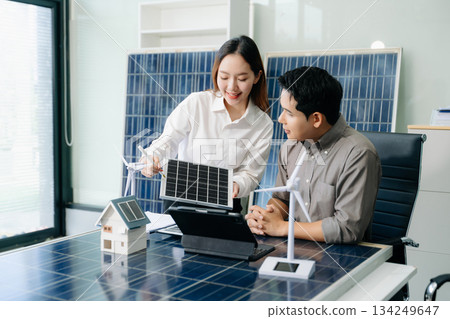 Two Asian engineers collaborate on a solar and wind energy project, discussing innovation and sustainability in a modern office setting. Two Asian engineers collaborate on a solar and wind energy project, discussing innovation and sustainability in a modern office setting. 134249647