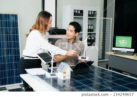 Two Asian engineers collaborate on a solar and wind energy project, discussing innovation and sustainability in a modern office setting. Two Asian engineers collaborate on a solar and wind energy project, discussing innovation and sustainability in a modern office setting. 134249657