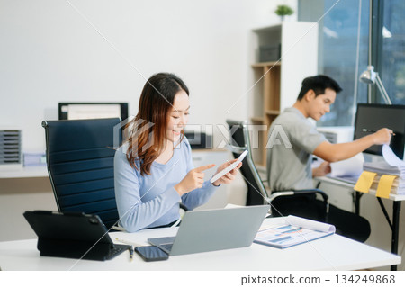 Asian woman smiling thinking planning writing in notebook, tablet and laptop working from home Asian woman smiling thinking planning writing in notebook, tablet and laptop working from home 134249868