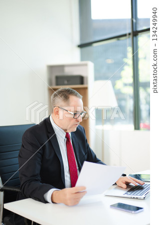 Mature businessman working in office with laptop, tablet, and notes. Perfect for business, finance, accounting 134249940