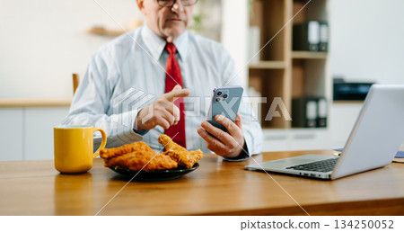 Mature Businessman using laptop while sitting at home. man sitting in kitchen Mature Businessman using laptop while sitting at home. man sitting in kitchen 134250052