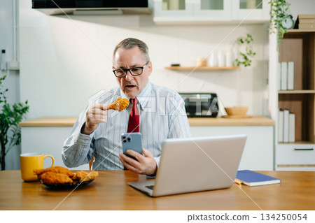 Mature Businessman using laptop while sitting at home. man sitting in kitchen and doing market research working 134250054