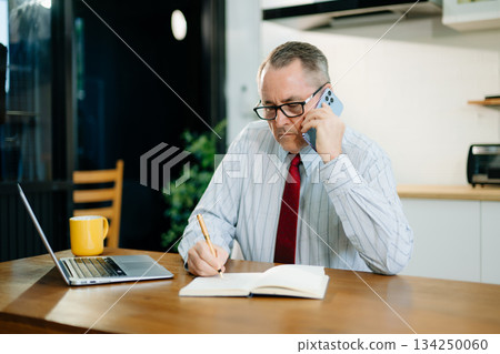 Mature Businessman using laptop while sitting at home. man sitting in kitchen 134250060