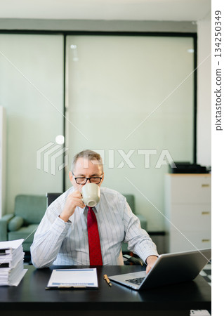 Mature businessman working in office with laptop, tablet, and notes. Perfect for business, finance, accounting Mature businessman working in office with laptop, tablet, and notes. Perfect for business, finance, accounting 134250349