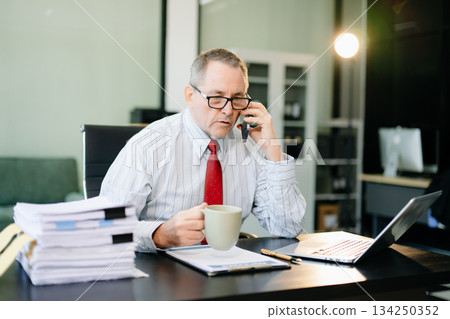 Mature businessman working in office with laptop, tablet, and notes. Perfect for business, finance, accounting Mature businessman working in office with laptop, tablet, and notes. Perfect for business, finance, accounting 134250352