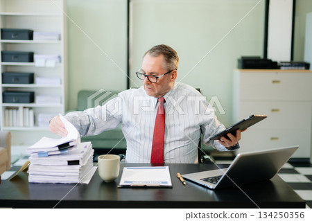 Professional businessman working at office with laptop, tablet, and notes. Perfect for business, finance Professional businessman working at office with laptop, tablet, and notes. Perfect for business, finance 134250356