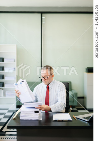 Professional businessman working at office with laptop, tablet, and notes. Perfect for business, finance Professional businessman working at office with laptop, tablet, and notes. Perfect for business, finance 134250358