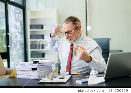 Angry and irritated Mature Businessman sitting in the office of laptop with his keyboard tired from work. Overwork, stress Angry and irritated Mature Businessman sitting in the office of laptop with his keyboard tired from work. Overwork, stress 134250359