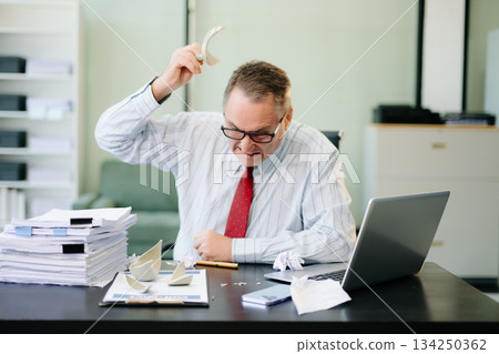 Angry and irritated Mature Businessman sitting in the office of laptop with his keyboard tired from work. Overwork, stress Angry and irritated Mature Businessman sitting in the office of laptop with his keyboard tired from work. Overwork, stress 134250362