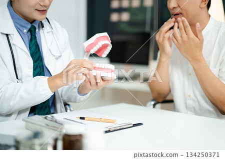 Dentist explaining dental health to male patient using model jaw. Oral care, tooth pain consultation, anatomy education 134250371