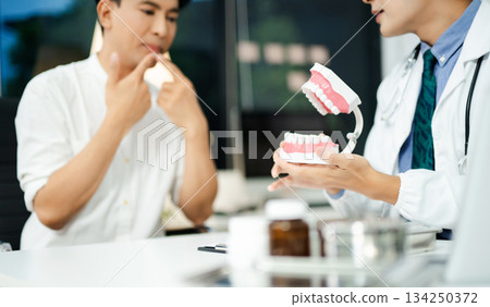 Dentist explaining dental health to male patient using model jaw. Oral care, tooth pain consultation, anatomy education 134250372