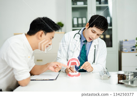 Dentist explaining dental health to male patient using model jaw. Oral care, tooth pain consultation, anatomy education Dentist explaining dental health to male patient using model jaw. Oral care, tooth pain consultation, anatomy education 134250377