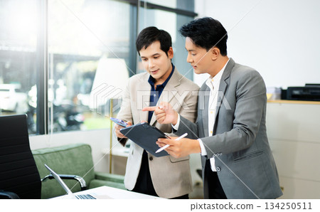 Two Asian businessmen using tablet and smartphone for project planning in a modern office. 134250511