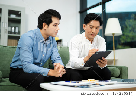 Happy Asian business partners collaborating on startup ideas using tablet and laptop in modern office. 134250514