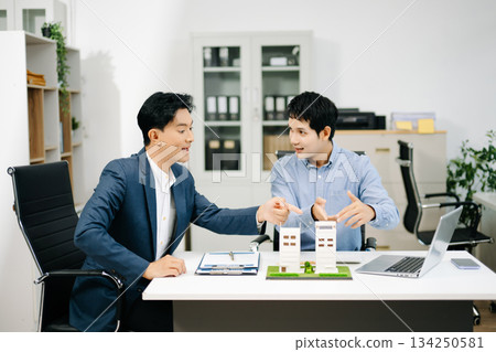Two professional men analyzing house model and design layout in office. Ideal for themes of architecture, investment, real estate, property Two professional men analyzing house model and design layout in office. Ideal for themes of architecture, investment, real estate, property 134250581