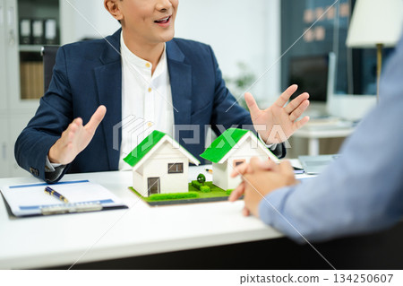 Real estate agent consulting with buyer on house model and pricing using calculator in modern office. and client service. Real estate agent consulting with buyer on house model and pricing using calculator in modern office. and client service. 134250607
