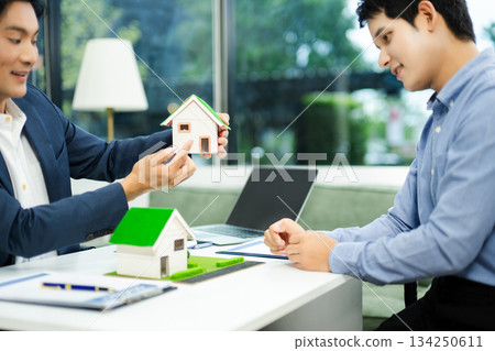 Real estate agent consulting with buyer on house model and pricing using calculator in modern office. and client service. Real estate agent consulting with buyer on house model and pricing using calculator in modern office. and client service. 134250611