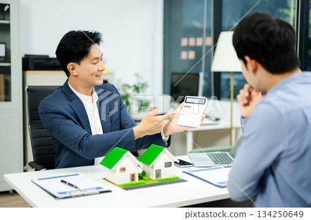 Real estate agent consulting with buyer on house model and pricing using calculator in modern office. and client service. Real estate agent consulting with buyer on house model and pricing using calculator in modern office. and client service. 134250649